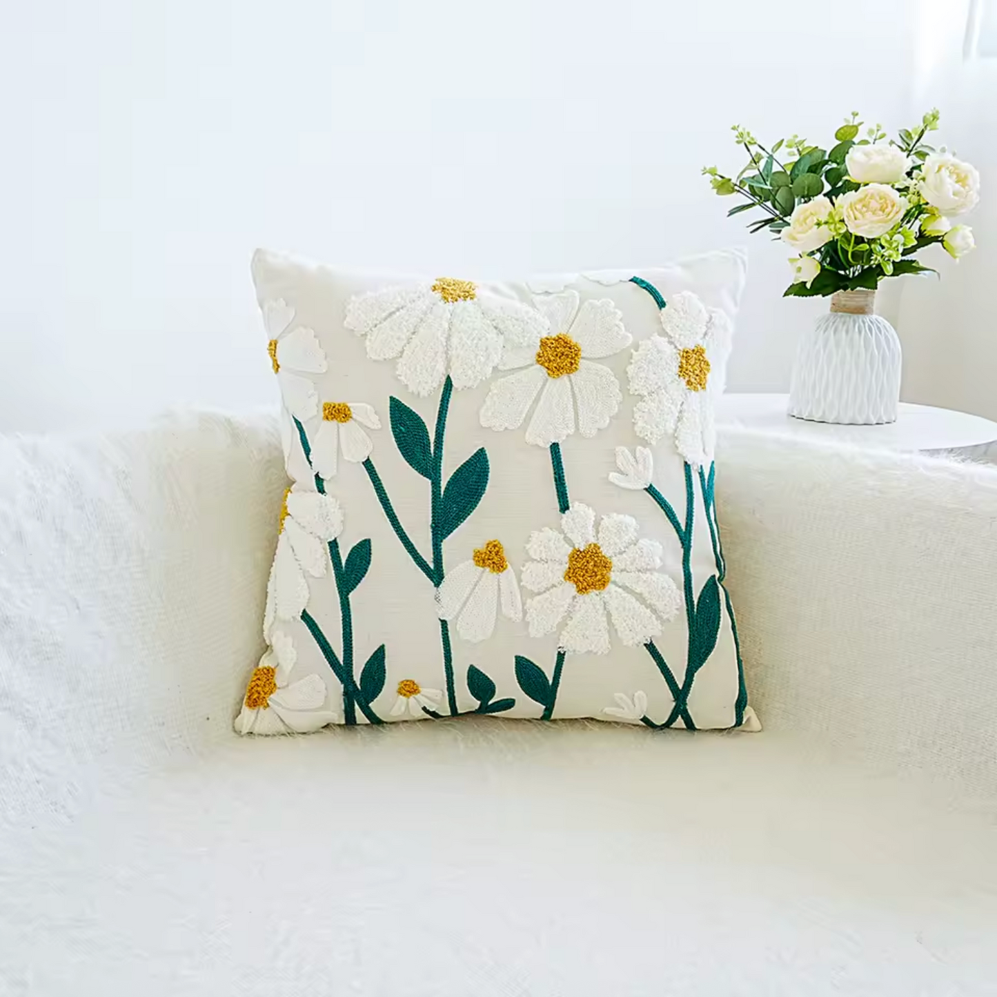 The Square Plantish Embroidered Daisy Cushion Cover in Big Daisy design, positioned on a white sofa with a vase of flowers on a table beside it.