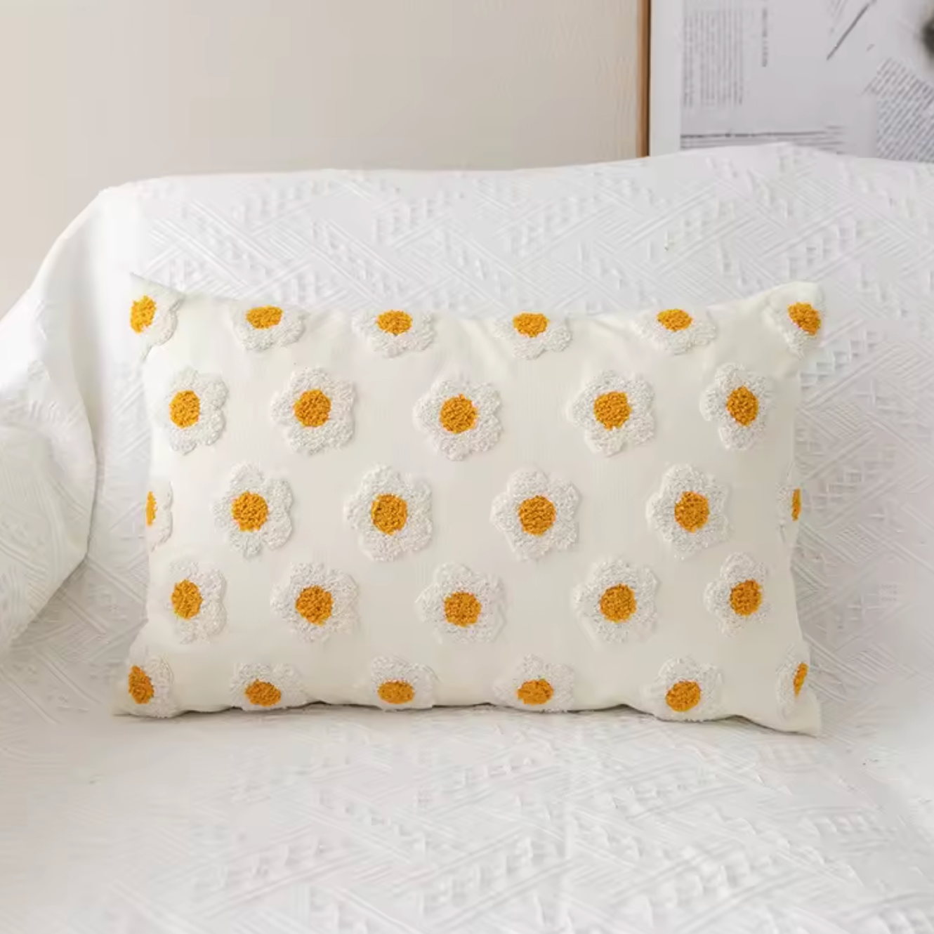 The Rectangular Plantish Embroidered Daisy Cushion Cover in Tiny Daisy design, positioned on a white sofa with a vase of flowers on a table beside it.