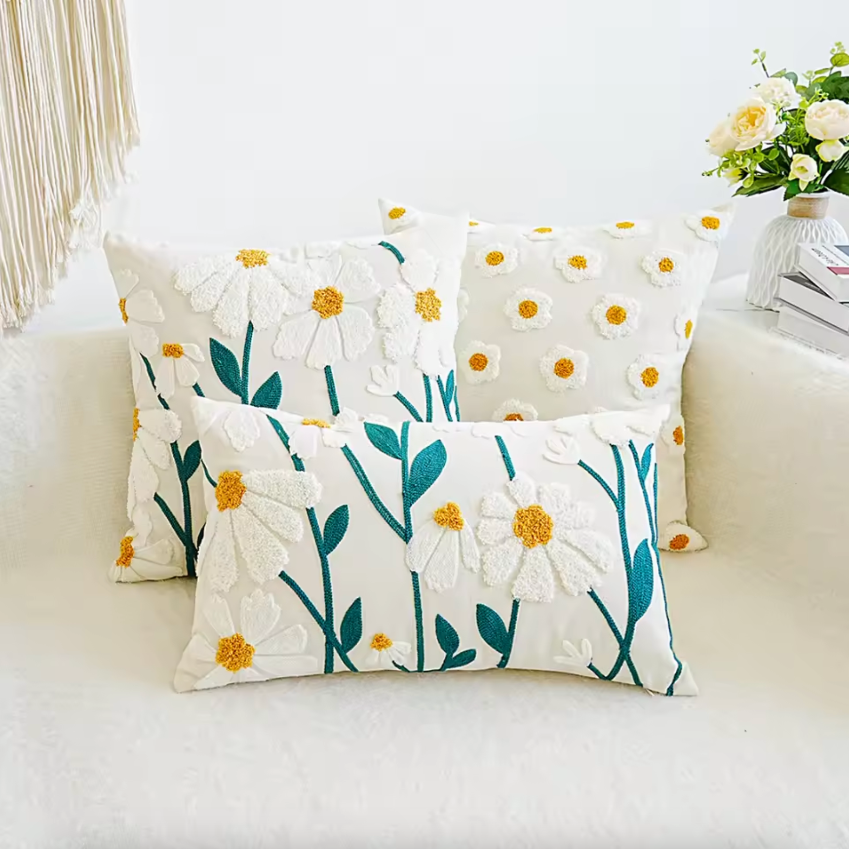 An image showing the Plantish Embroidered Daisy Cushion Cover in three different sizes resting on a white sofa, next to a table with books and flowers on.