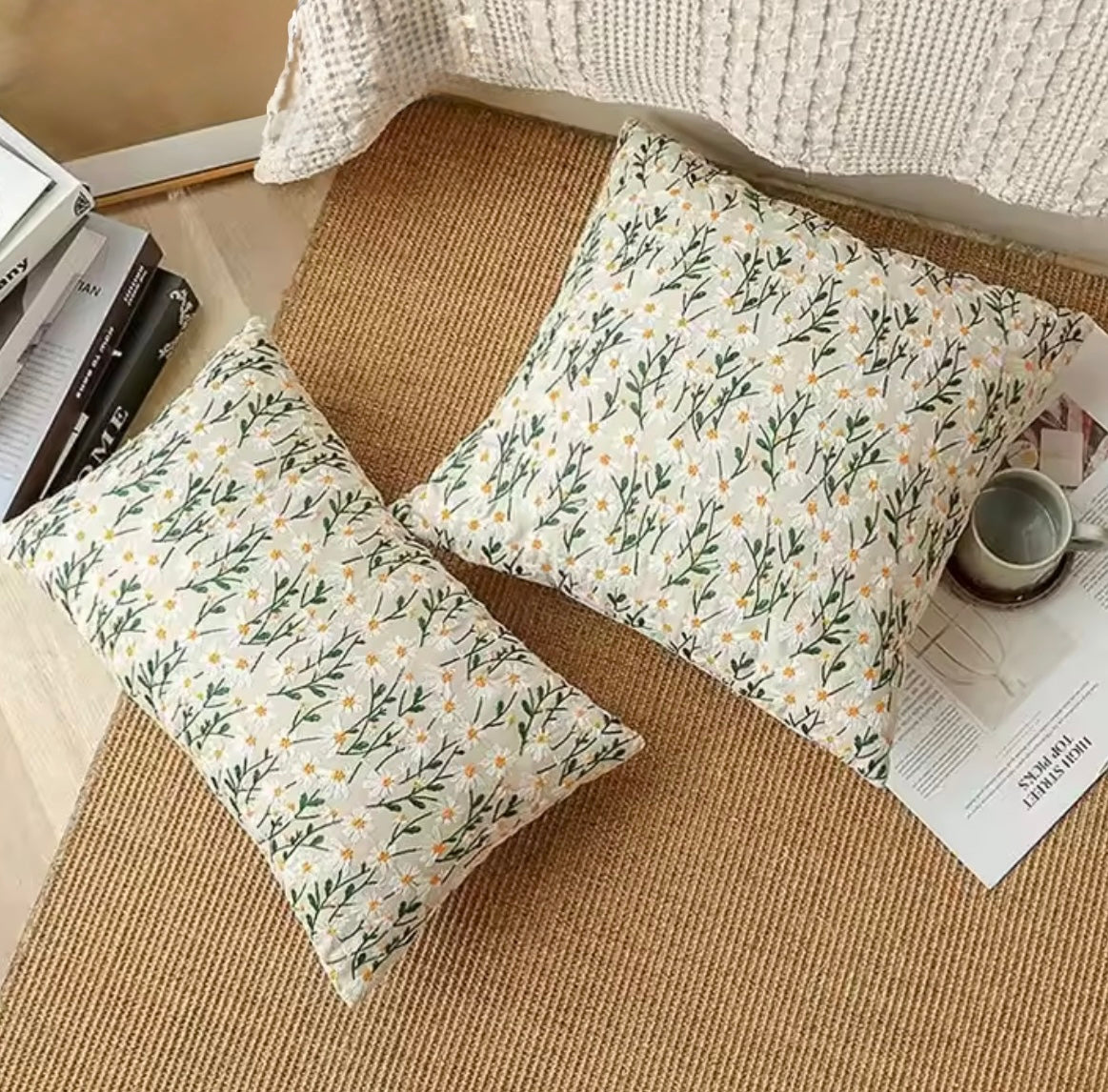 Both sizes of the Plantish Embroidered Little Daisy Cushion shown on a brown hessian rug which is on the floor of a stylish house. 
