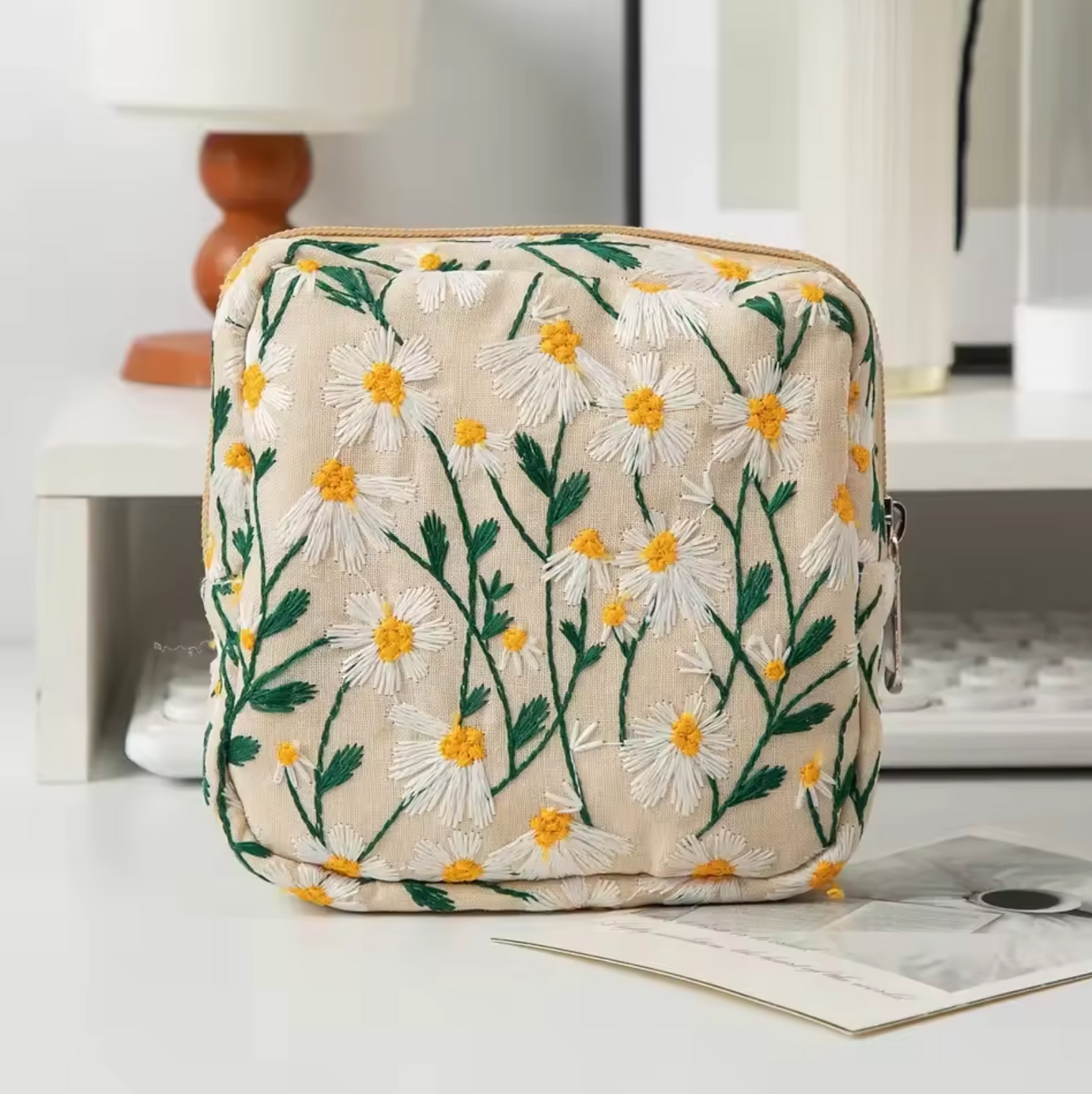 The Plantish Embroidered Little Daisy Makeup Bag 13.5cm x13.5cm x 5cm in Linen, shown on a white desk with assorted stationary.
