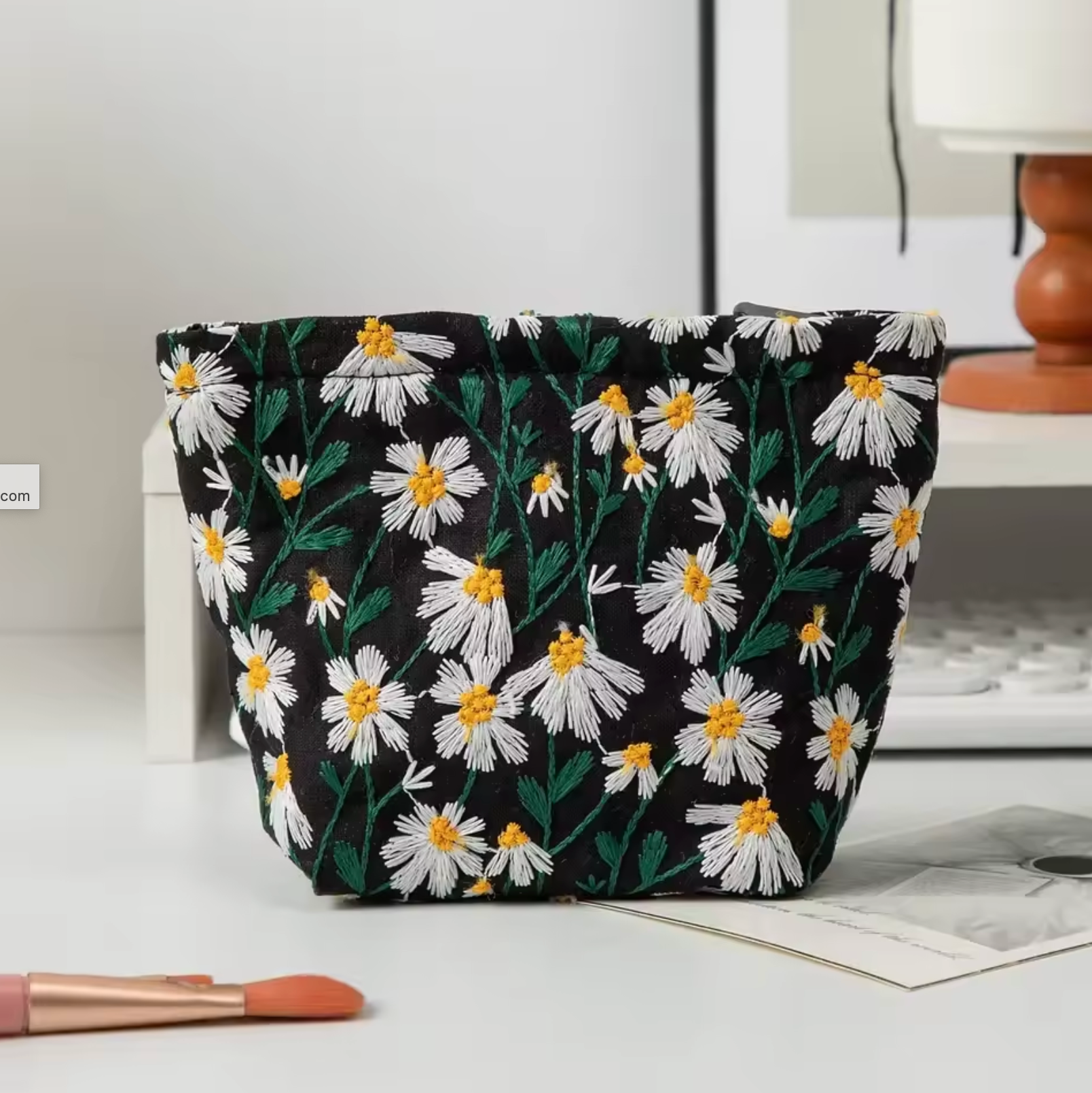 The Plantish Embroidered Little Daisy Makeup Bag 16cm x 6cm x1 2.5cm in Black, shown on a white desk wit h a keyboard visbile.