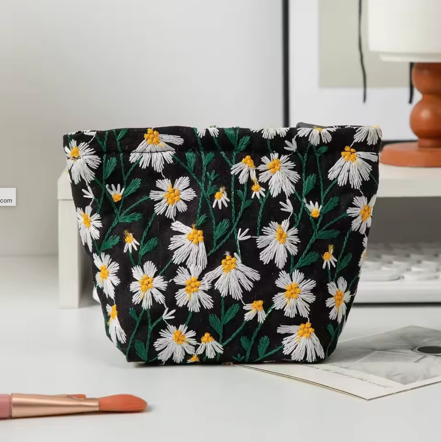 The Plantish Embroidered Little Daisy Makeup Bag 16cm x 6cm x1 2.5cm in Black, shown on a white desk wit h a keyboard visbile.