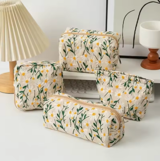 The Plantish Embroidered Little Daisy Makeup Bag in Linen shown in four different shapes, on a white desk with assorted stationary.
