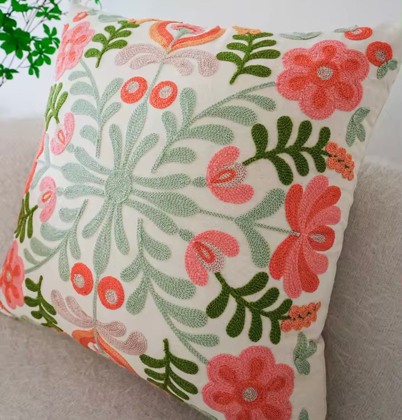 The Plantish Embroidered Sage Flower Cushion, shown on a grey sofa with a green plant in the background, as well s  white wall.
