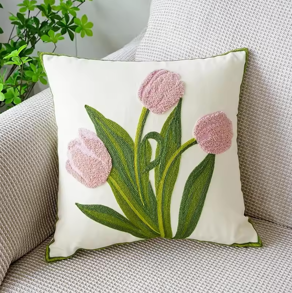 The Plantish Embroidered Tulip Cushion Cover, shown in Pink and positioned on a grey sofa with a green plant visible in the corner. 