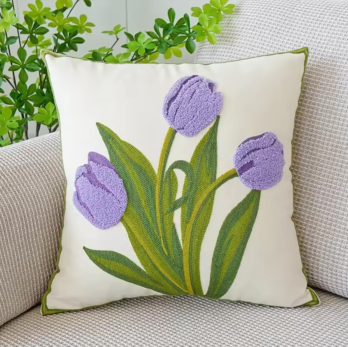 The Plantish Embroidered Tulip Cushion Cover, shown in Purple and positioned on a grey sofa with a green plant visible in the corner. 