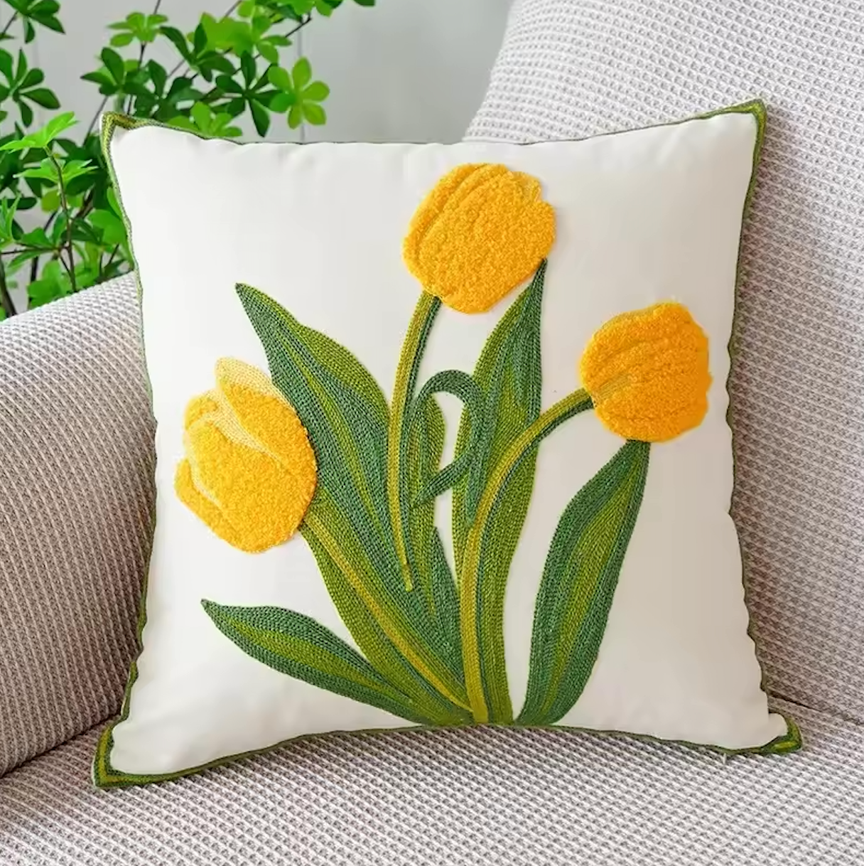 The Plantish Embroidered Tulip Cushion Cover, shown in Yellow and positioned on a grey sofa with a green plant visible in the corner. 
