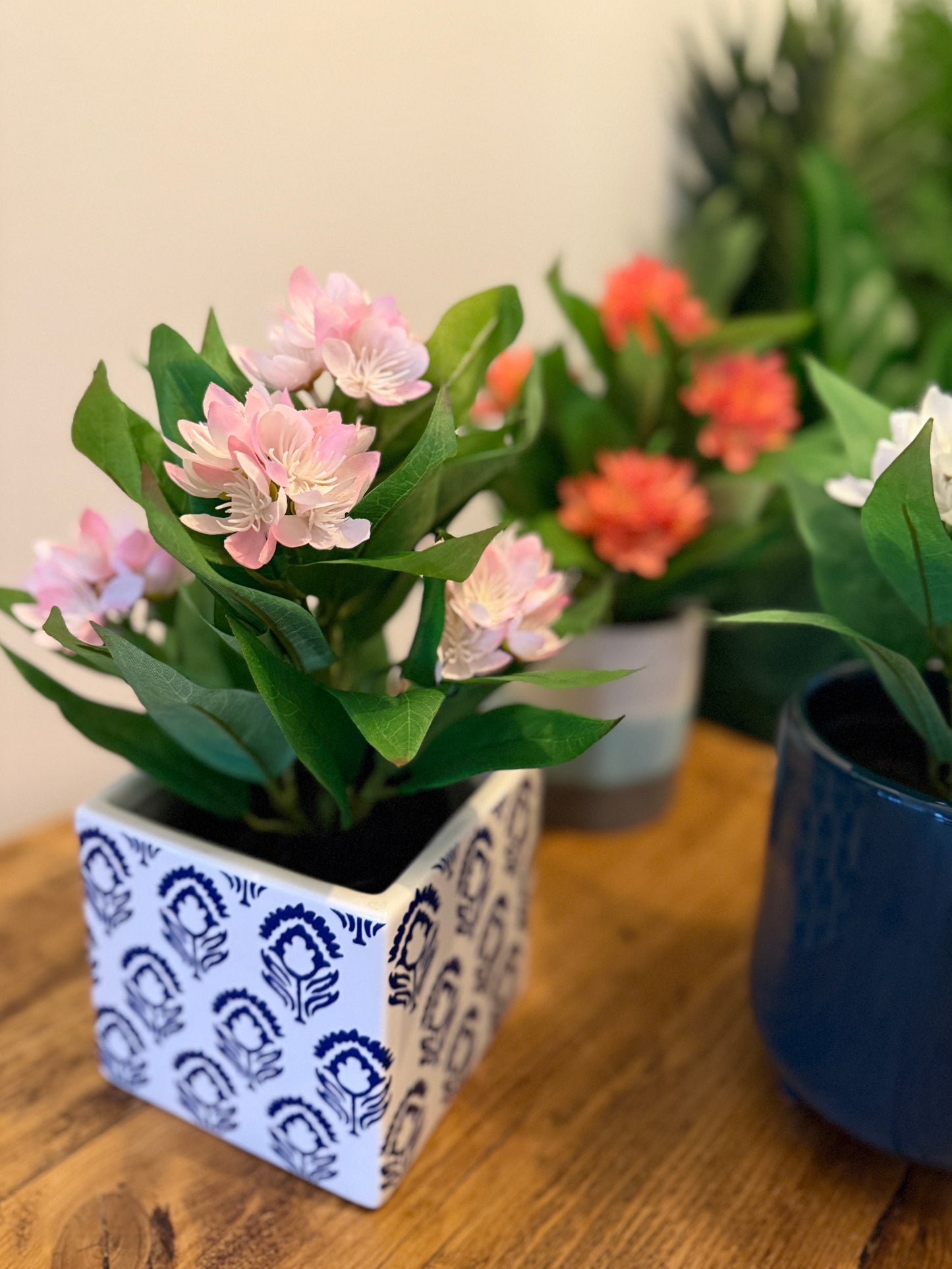 Close up of the Plantish artificial Freesia with light pink flowers in the foreground, and white and orange variants in the background. All of the plants are in ceramic pots. 