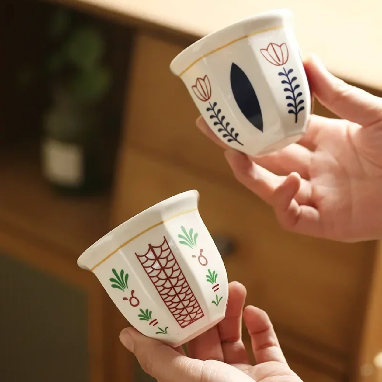 Both designs of the Plantish Floral Espresso Cup Set being held in a womans hands. There is one in the Leaf design and one in the Flower design.
