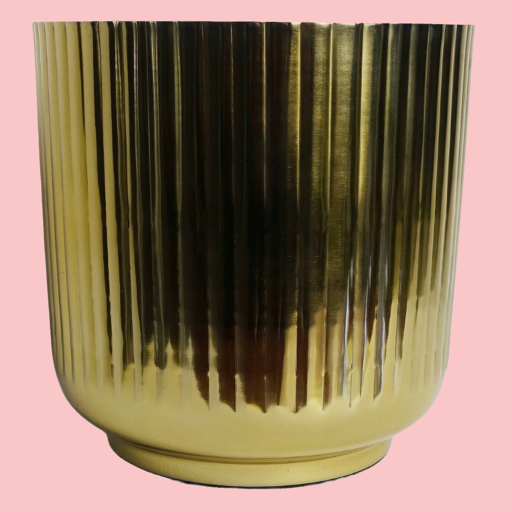 Side view of the Plantish Gold Ridged Metal Pot, highlighting the vertical ridge design, shown on a block pink background.