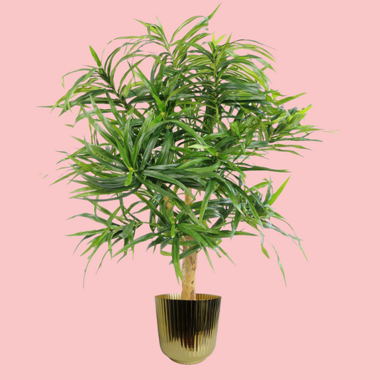 Side view of the Plantish Gold Ridged Metal Pot, with an artificial plant in the pot, shown on a block pink background.