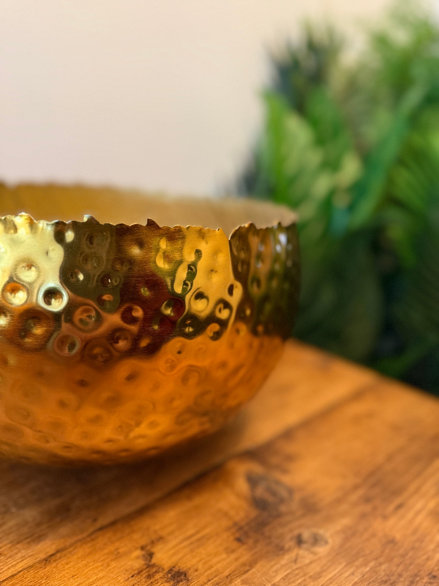Close up of a large hammered gold-coloured metal planter, highlighting its textured surface.