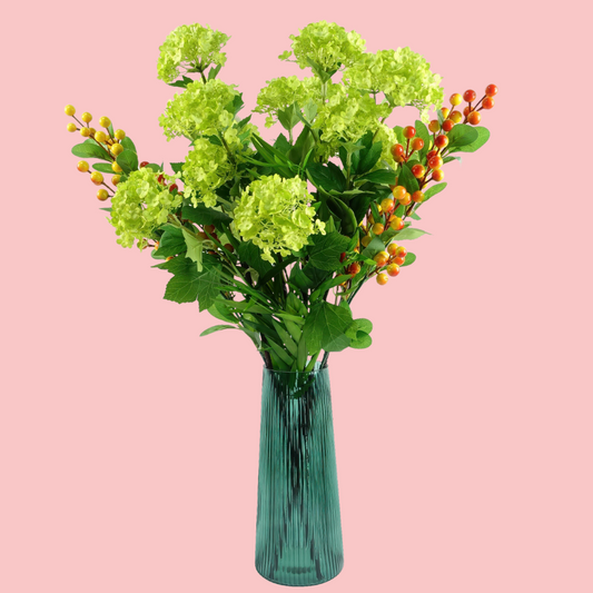 Side view of the Plantish Green Ridged Vase, highlighting the vertical ridge design. Shown with artificial flowers inside and on a block pink background.