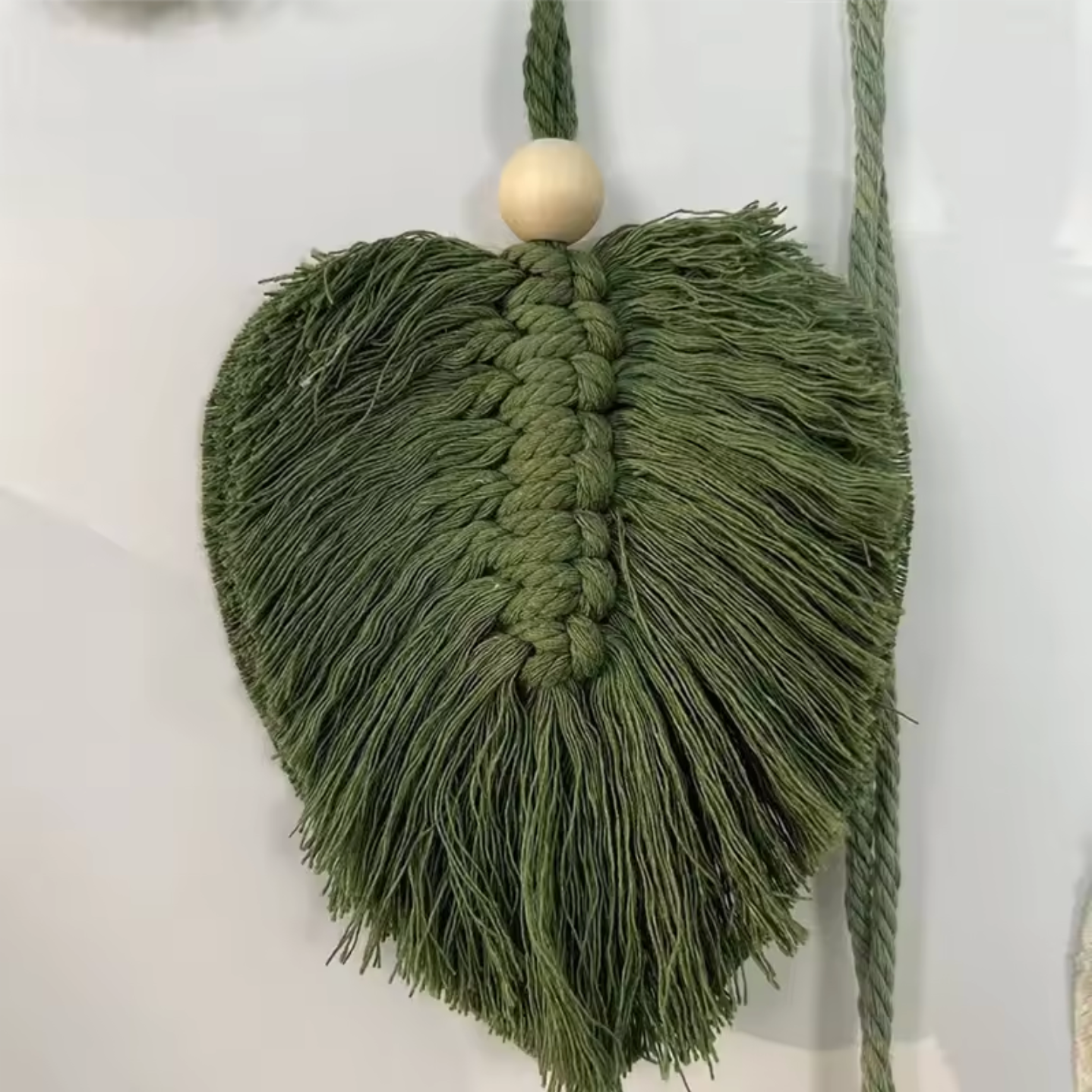 A close up of a cotton green leaf on the Plantish Hanging Leaf Macrame, highlighting the woven centre and shaped threads, attached to a thread with a bead.