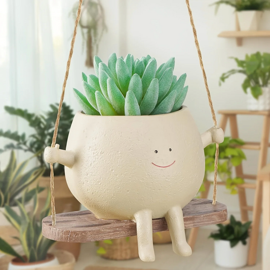 A close up of the Plantish Happy Swing Plant Pot, hanging inside a room with many plants. There is a green succulent inside the pot.