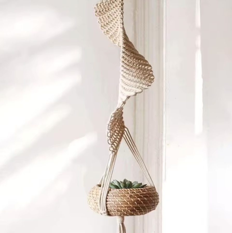 The Plantish Helix Macrame shown hanging with a rattan plant pot suspended inside of it, in front of a white background. There is a green succulent in the pot. 