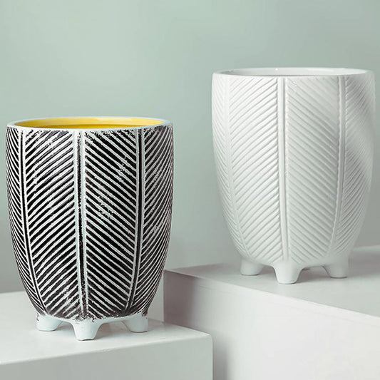 A view two ceramic plant pots with a zig zag herringbone design,  the left one is black and white and the right one is white, both have four small feet. 