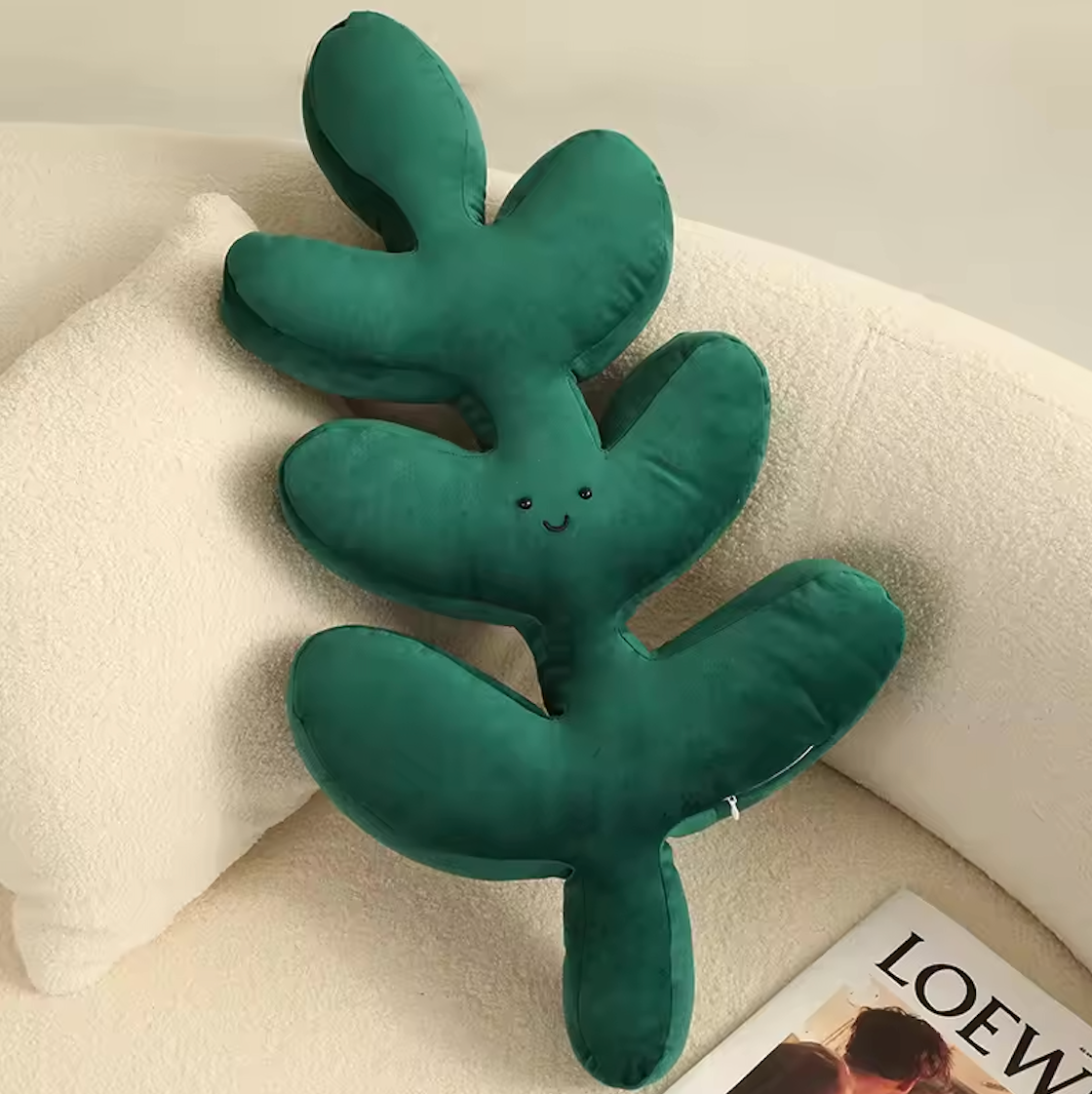 The Plantish Jungle Leaf Cushion Fern design. Shown in the corner of a white sofa, and highlighting the front design of the cushion, including a happy face.