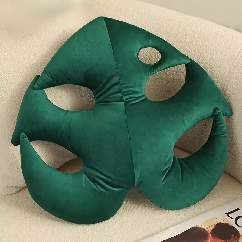 A close up of the Plantish Jungle Leaf Cushion in the Green Monstera Variant, shown resting on a fluffy beige sofa. 