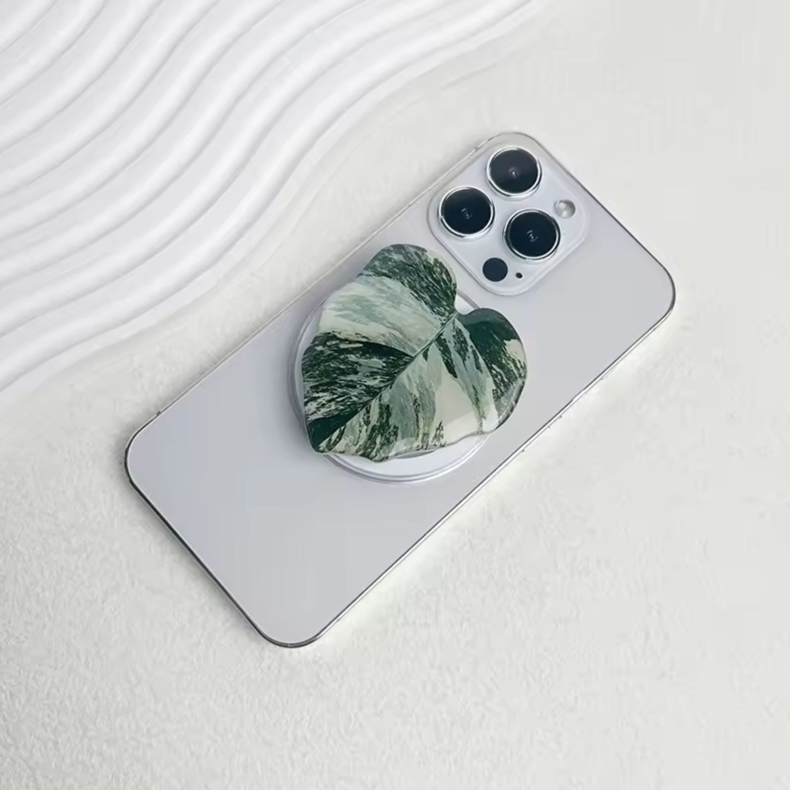 The Plantish White Princess leaf pop socket attached to the back of a white iPhone.