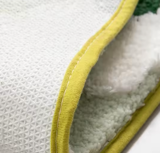 A close up image of underside of the Plantish Lush Moss Rug, showing the yellow edge seam and the grippy white underside made of rubber.