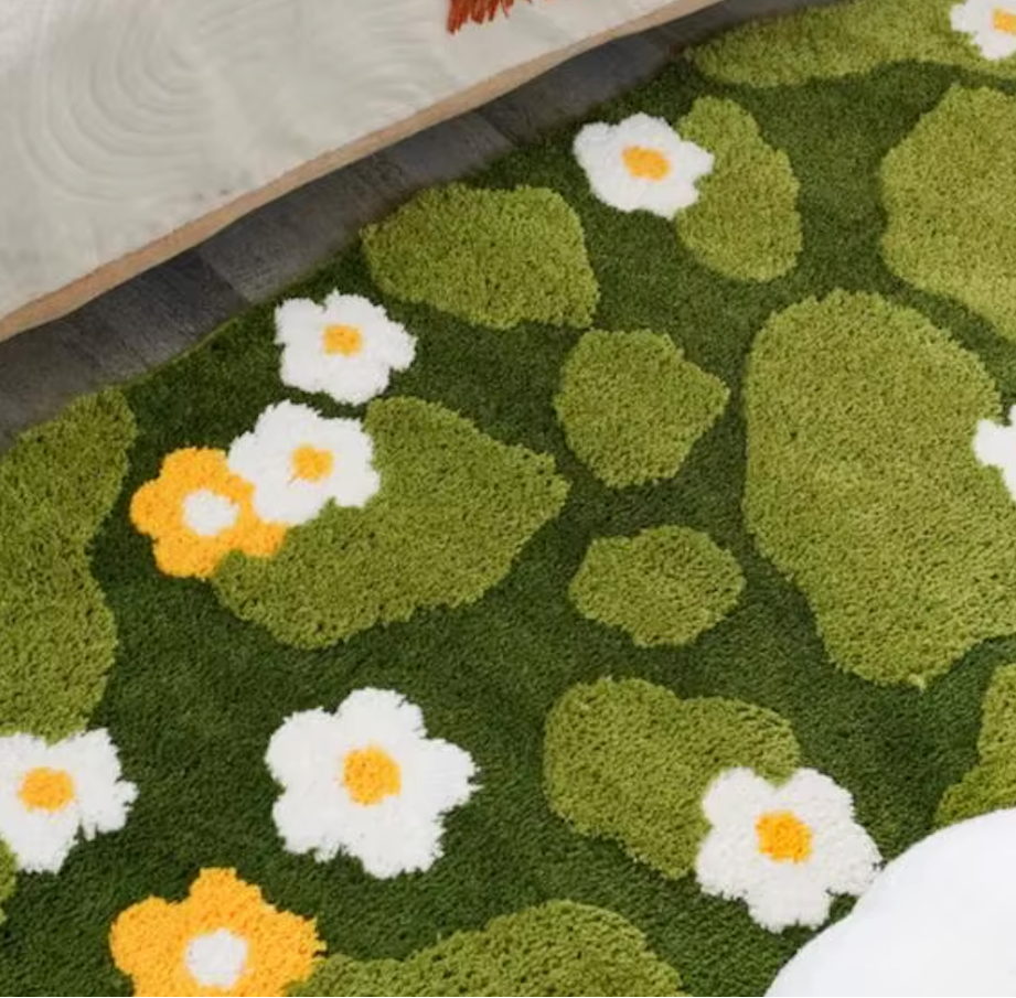 A close up image of the Plantish Mossy Daisies Rug on the floor of a bedroom. 