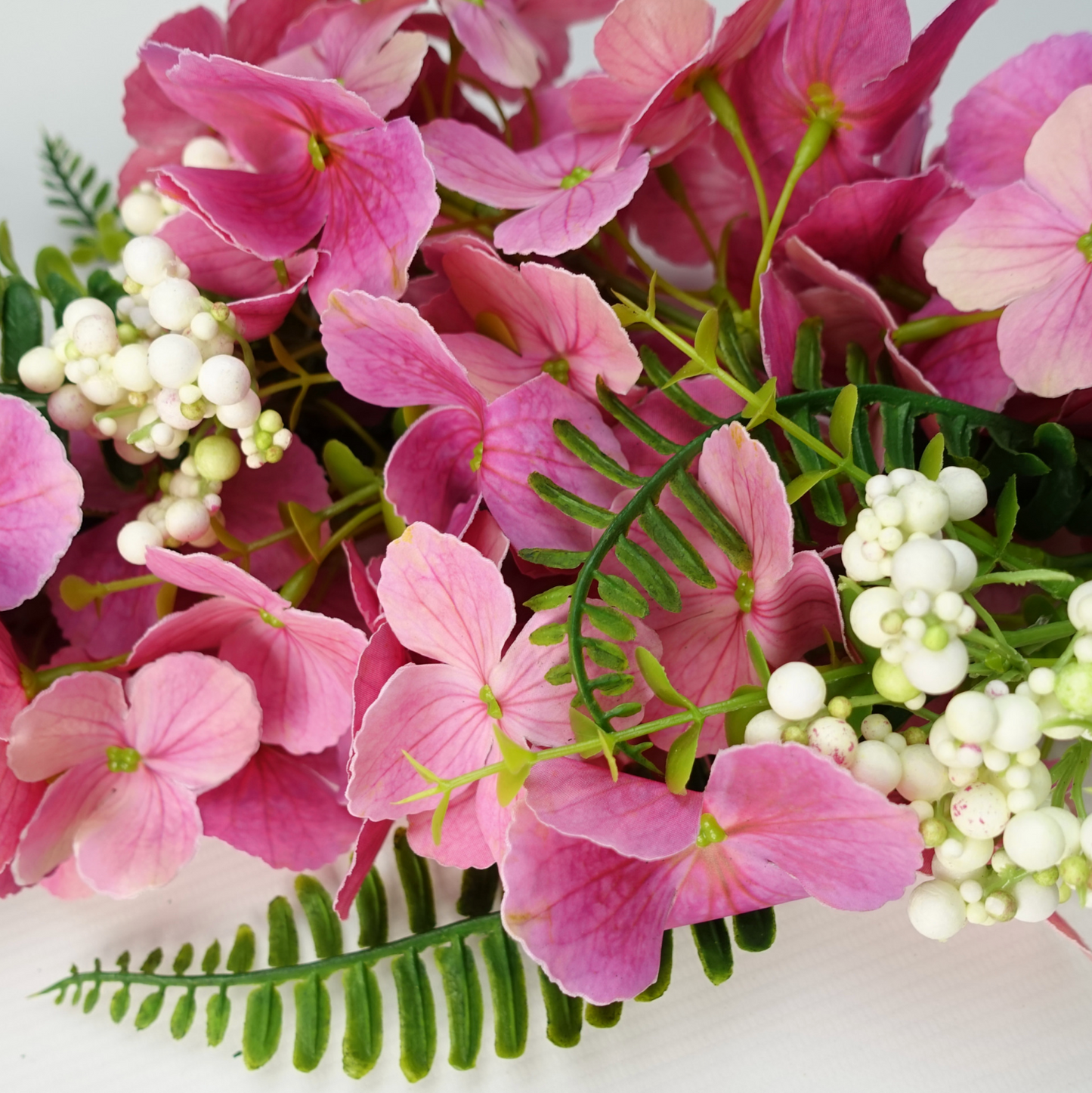 A close up of the Plantish Pink Cherry Blossom Garland, showing the vibrant pink flowers, green leaves, and white berries in detail. 