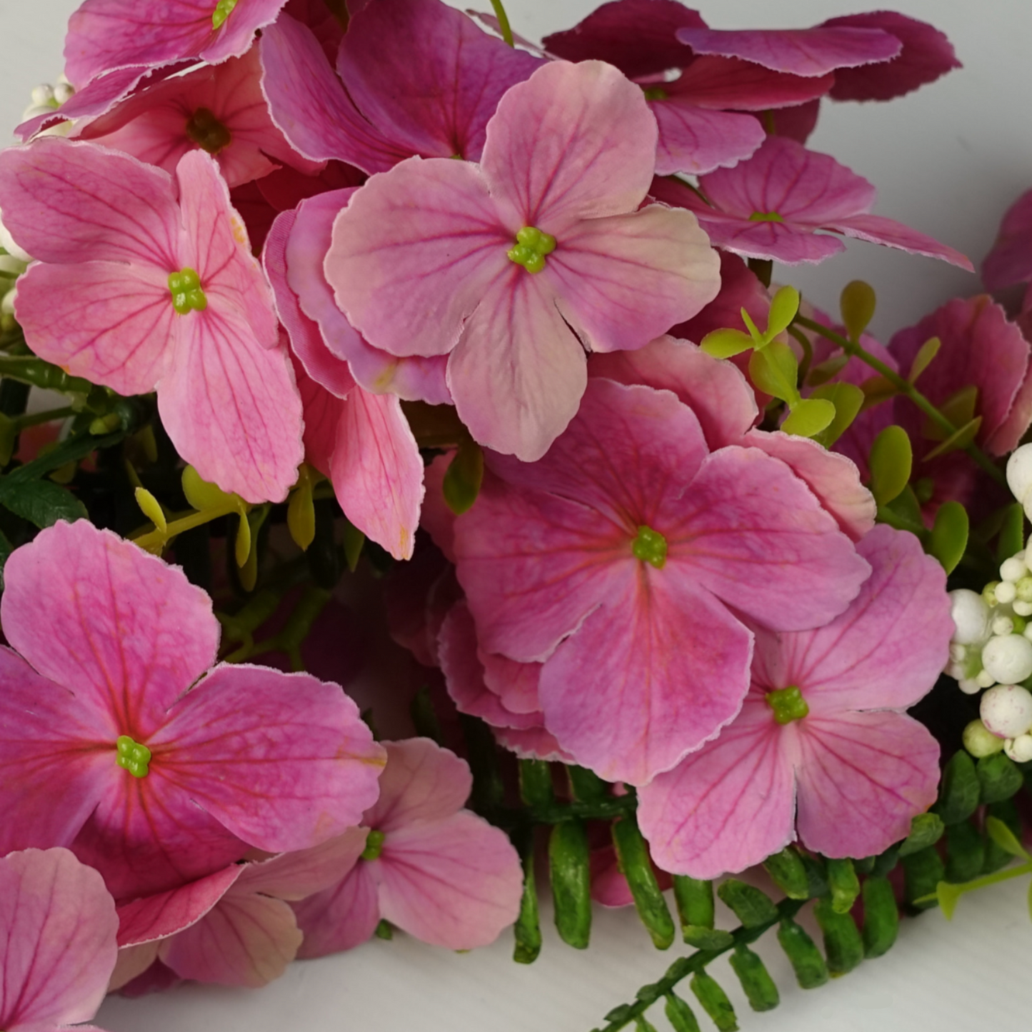 A close up of the Plantish Pink Cherry Blossom Garland, focusing on the vibrant pink flowers, with green leaf foliage also visible. 
