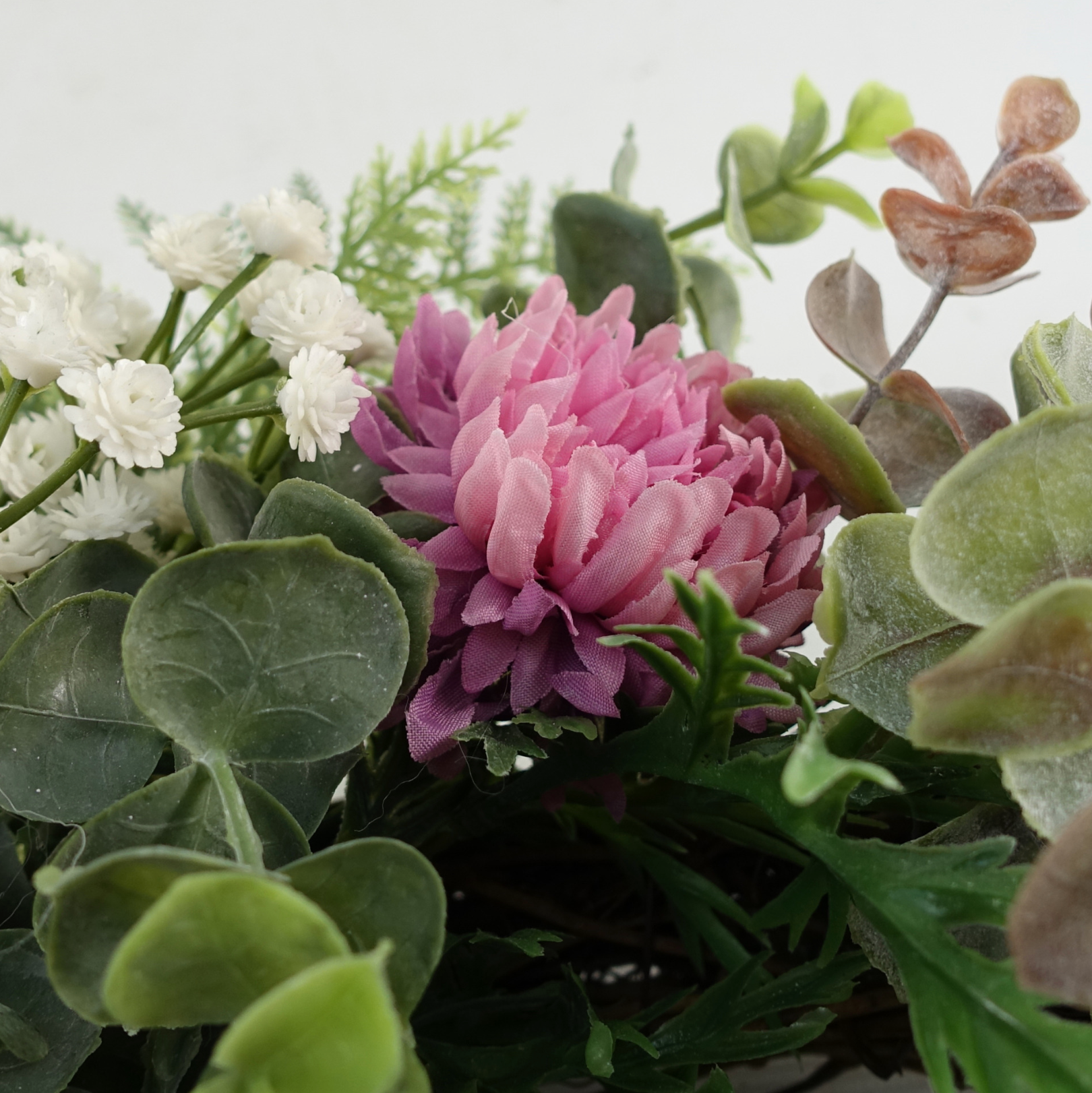 A close up of the Plantish 45cm Pink Peony Wreath, highlighting the pink peonies, green leaves and fronds, and small white flowers. 