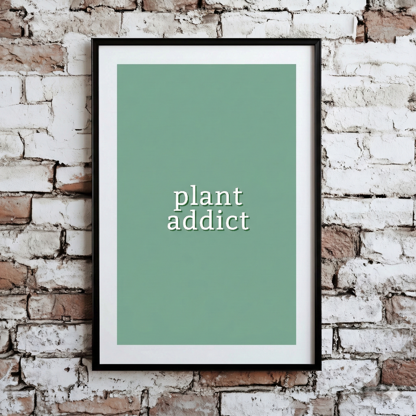 A Plantish print of the phrase "Plant Addict" in a white font with green background, shown hanging on a brick wall.