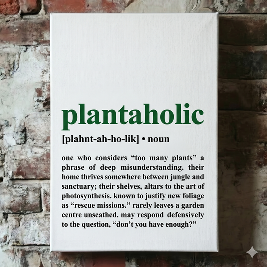 A Plantish canvas of the phrase "Plantaholic" in the style of a dictionary definition, showing the pronunciation against a white background, hanging on a red brick wall.