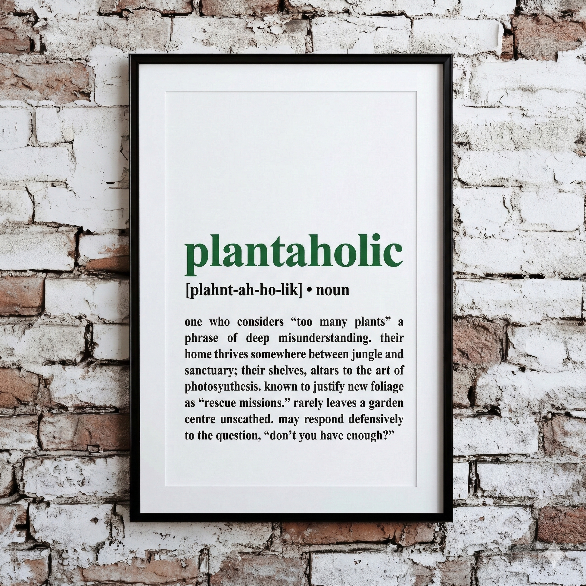 A Plantish print of the phrase "Plantaholic" in the style of a dictionary definition, showing the pronunciation against a white background, hanging on a brick wall.