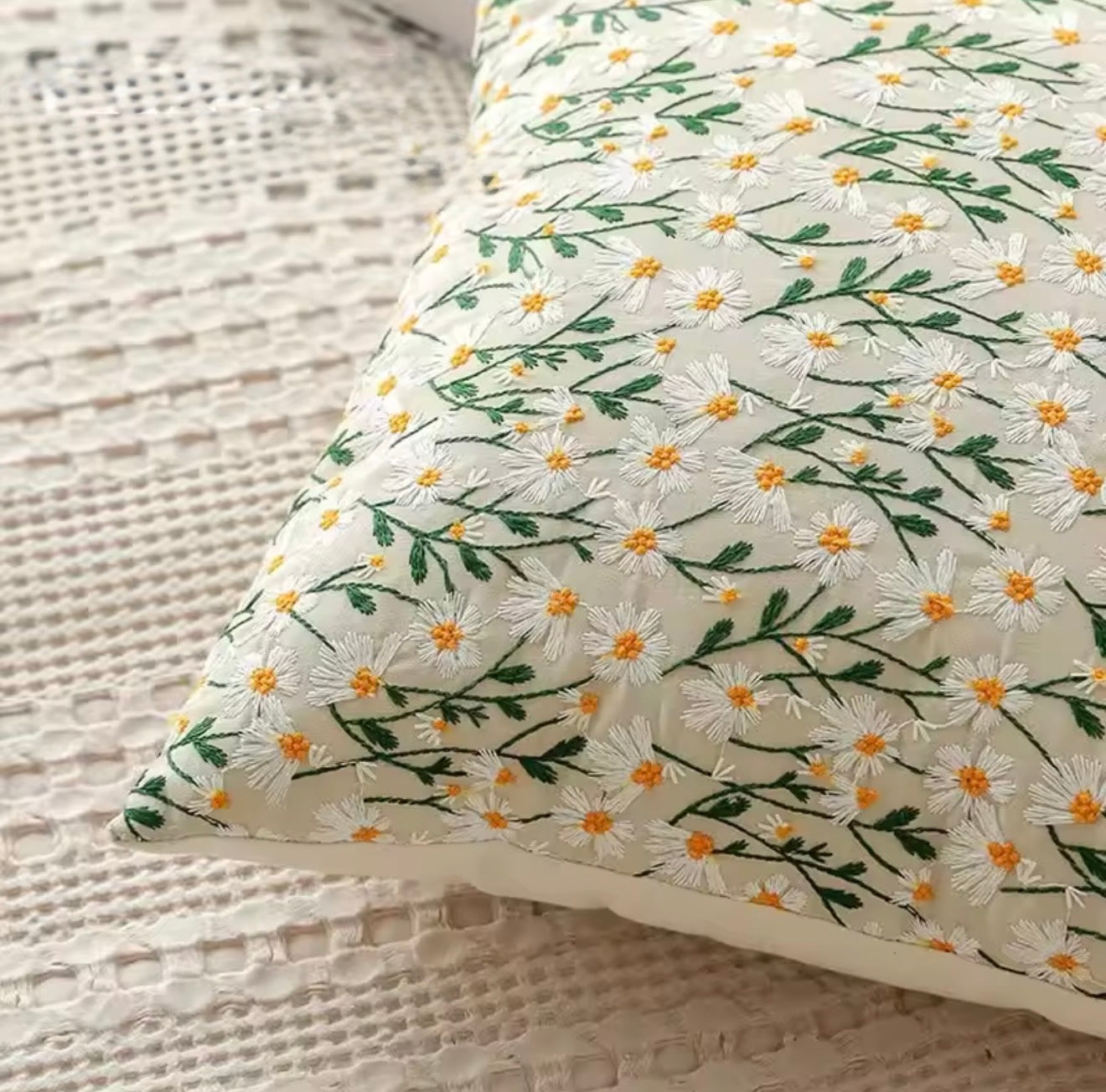 A close up of the Plantish Embroidered Little Daisy Cushion, highlighting the delicate white and yellow flowers and green stems design. 