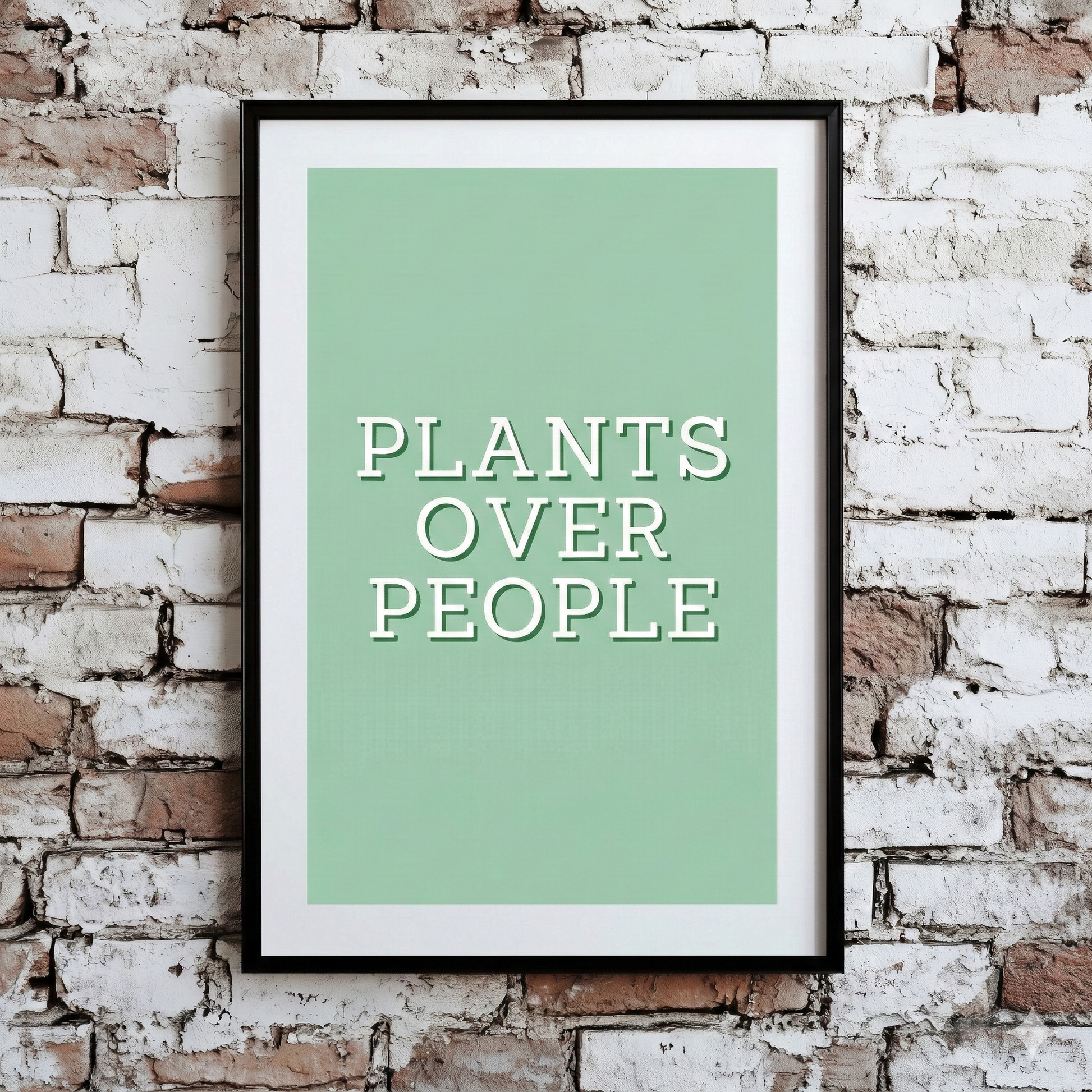 A Plantish print of the phrase "Plants Over People" in a white font with a green background, shown hanging on a brick wall.