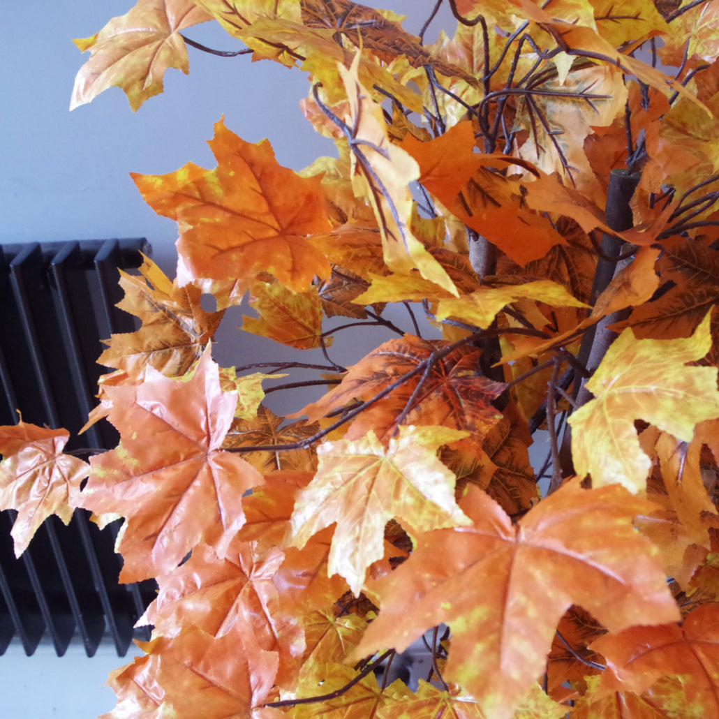 A close up of the orange leaves of the Plantish artificial maple tree, showing off the subtle orange, yellow and brown tones with a grey wall in the background. 