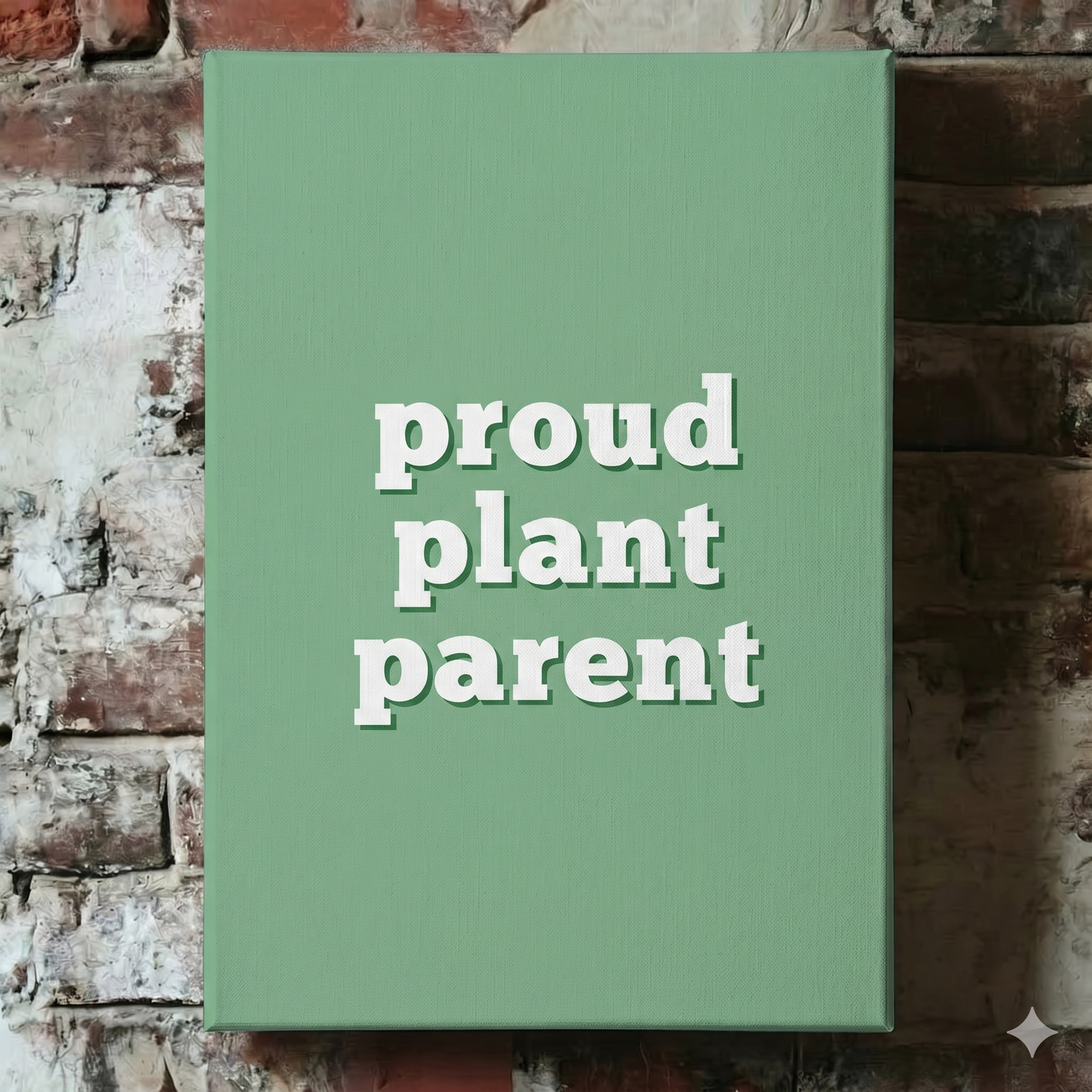 A Plantish canvas of the phrase "Proud Plant Parent" in a white font with a green background, shown hanging on a red brick wall.