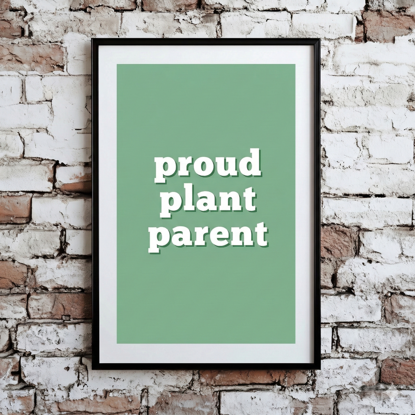 A Plantish print of the phrase "Proud Plant Parent" in a white font with a green background, shown hanging on a brick wall.