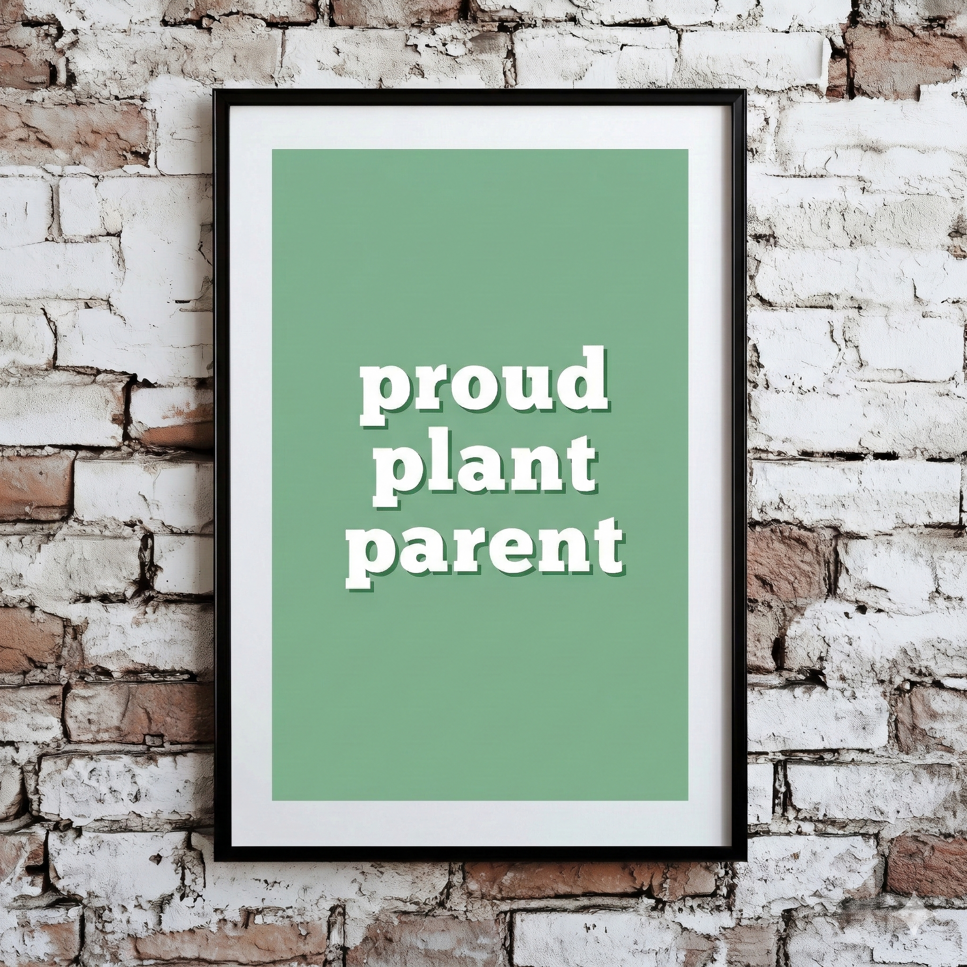 A Plantish print of the phrase "Proud Plant Parent" in a white font with a green background, shown hanging on a brick wall.