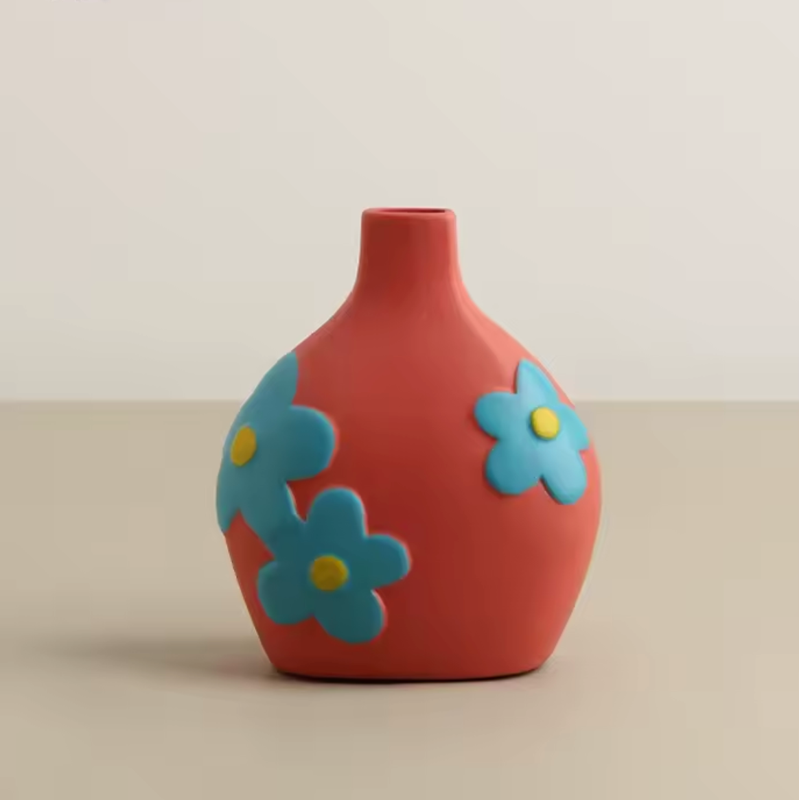 The Plantish Retro Floral Ceramic Vase in Coral, shown shown against a plain cream table and white wall. 
