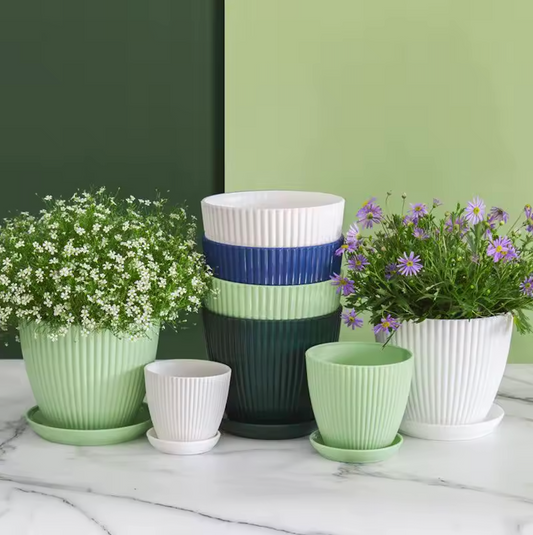 An image of the Plantish Ridged Plastic Planter in various colours and sizes, on a white marble table with a two toned green wall in the background.