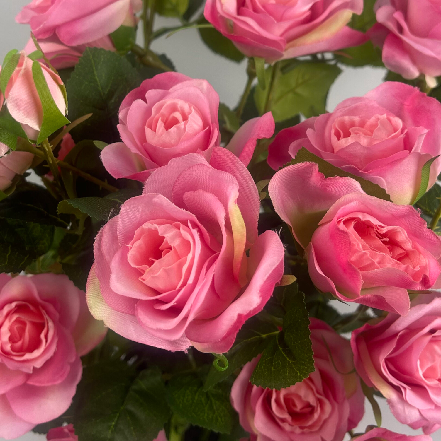 A close up of the Plantish artificial rose bush, showcasing the vibrant pink flowers and green leaves in high detail. 