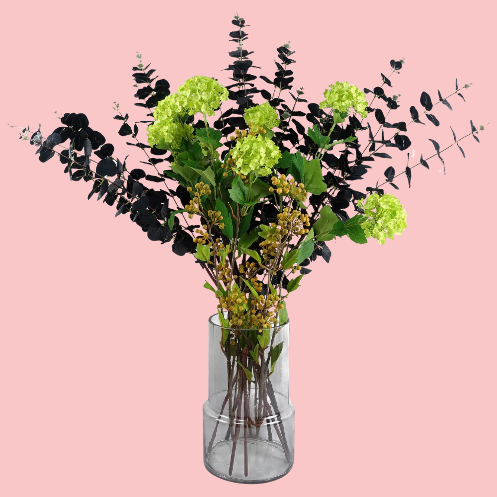 Side view of the Plantish Smoky Vase, made of smoked glass. Shown with artificial flowers inside and on a block pink background.