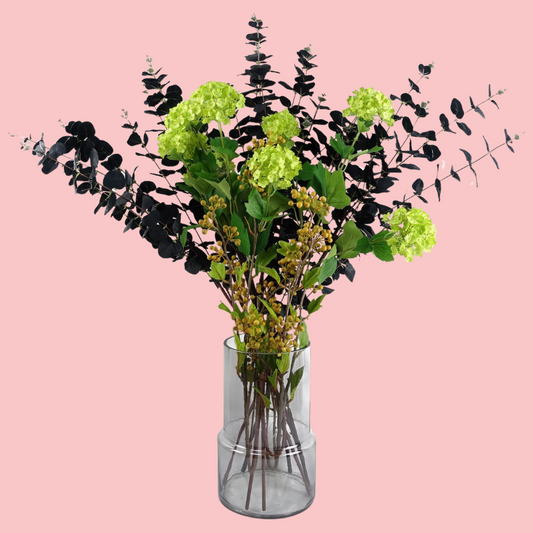 Side view of the Plantish Smoky Vase, made of smoked glass. Shown with artificial flowers inside and on a block pink background.