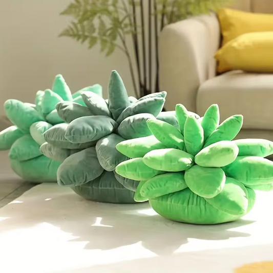 The Plantish Succulent Plush Cushion shown in Bright Green, Sage Green, and Mint Green in a sunlit living room. There's a plant and a sofa in the background. 