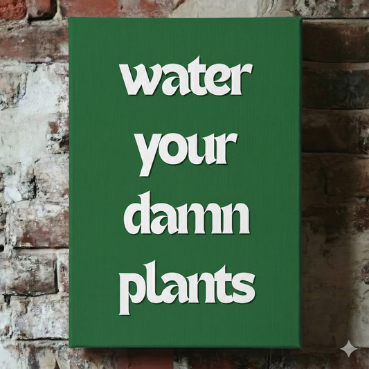 A Plantish canvas showing the phrase "Water Your Damn Plants" in a white font against a green background, hanging on a red brick wall.