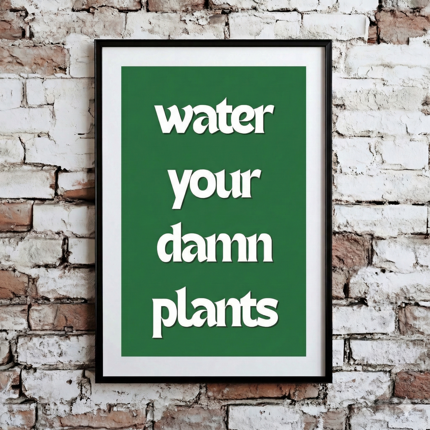 A Plantish print showing the phrase "Water Your Damn Plants" in a white font against a green background, hanging on a brick wall.