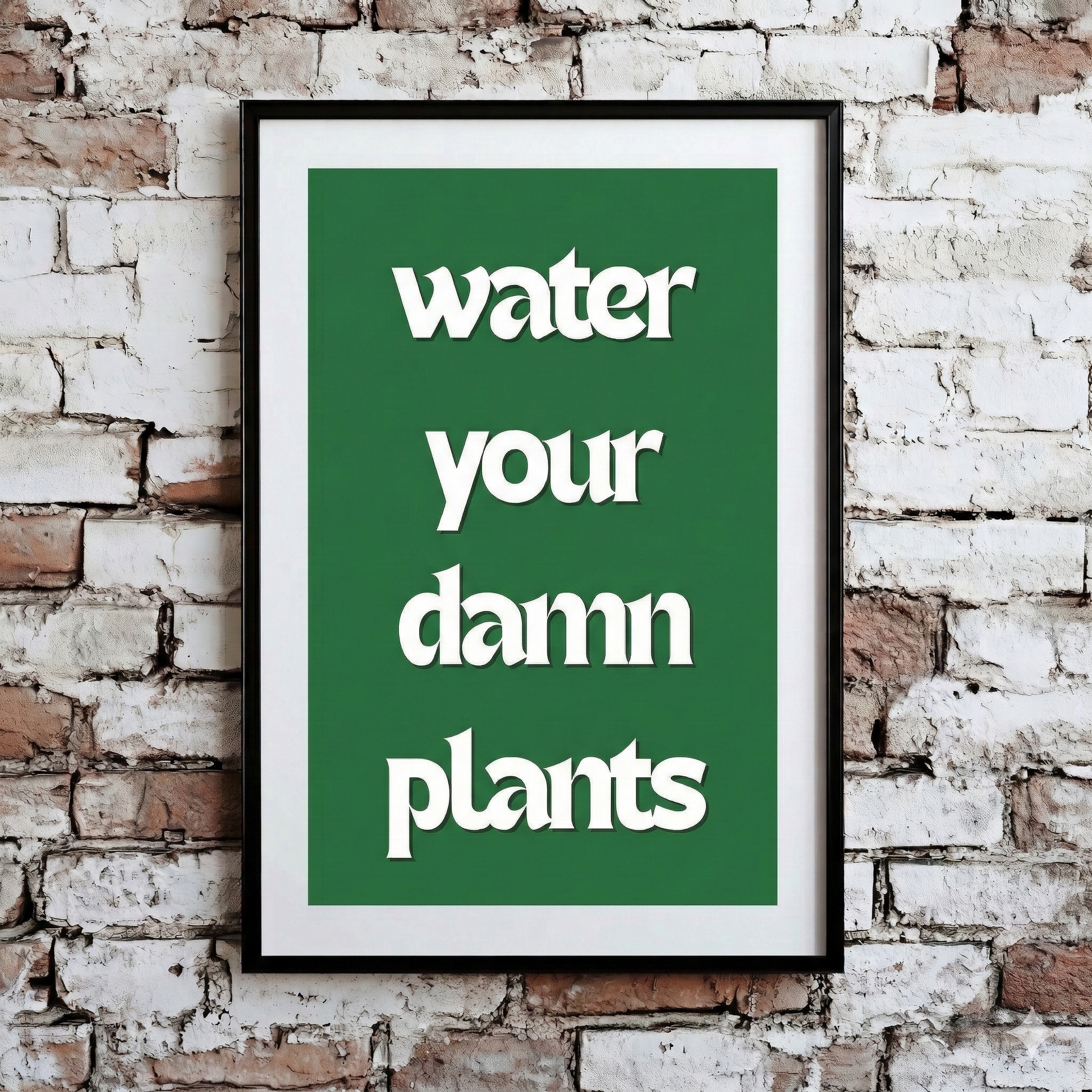 A Plantish print showing the phrase "Water Your Damn Plants" in a white font against a green background, hanging on a brick wall.