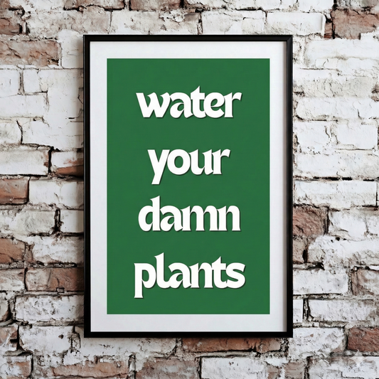 A Plantish print showing the phrase "Water Your Damn Plants" in a white font against a green background, hanging on a brick wall.