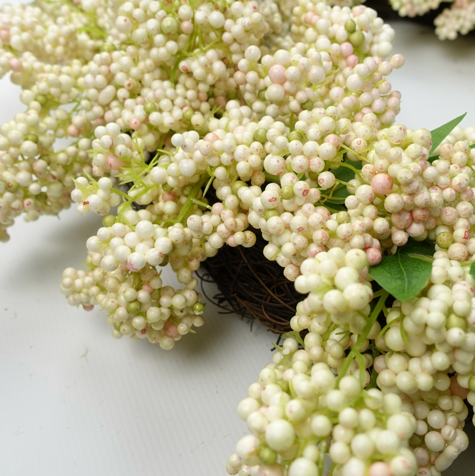 A close up of the Plantish 55cm White Berry Wreath, detailing the white berries and green leaves, as well as some of the woven ring. 